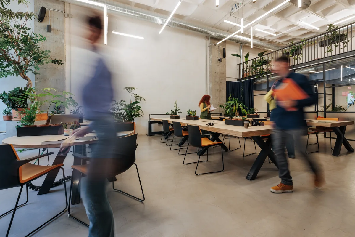 Pessoas circulando em um ambiente de trabalho compartilhado, com mesas e plantas